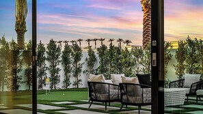A patio with outdoor furniture, a well-maintained lawn, and a row of tall plants against a wall. - 2 Luxury Villas Pickleball Court, Pool, Putting Green Bravo by Avantstay (Indio)