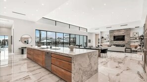A modern kitchen with a large island, wooden cabinets, and a view through large windows. - 2 Luxury Villas Pickleball Court, Pool, Putting Green Bravo by Avantstay (Indio)