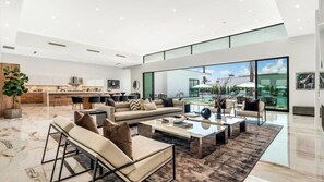 A spacious living area with a large sofa, coffee table, and a view of a pool and outdoor seating. - 2 Luxury Villas Pickleball Court, Pool, Putting Green Bravo by Avantstay (Indio)