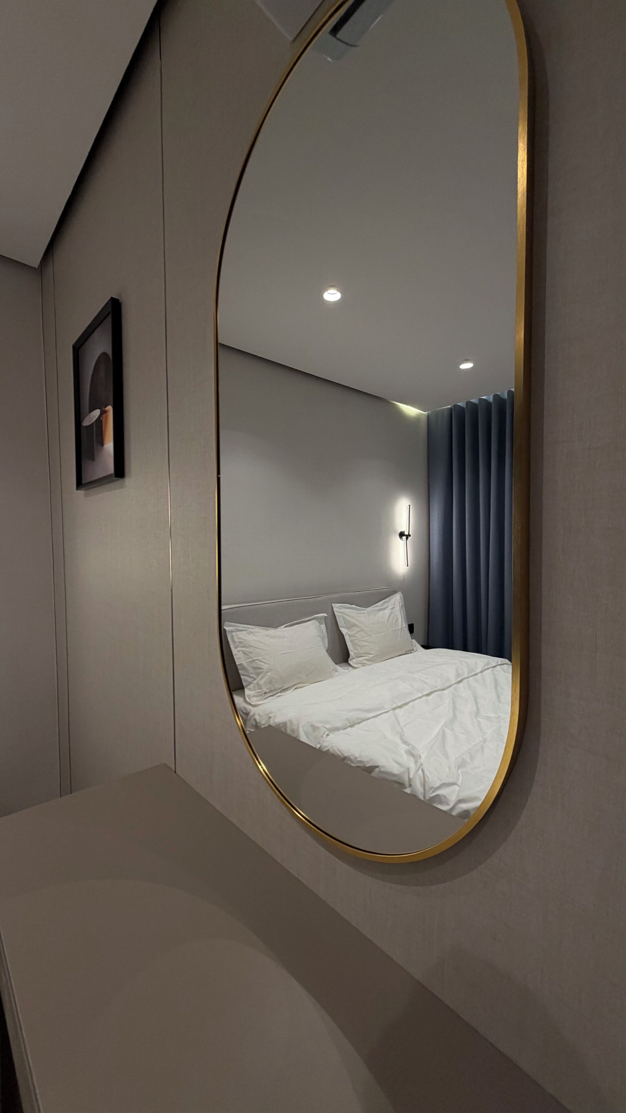 Et hotelværelse med en seng, et natbord, et spejl og en vægmonteret lampe.