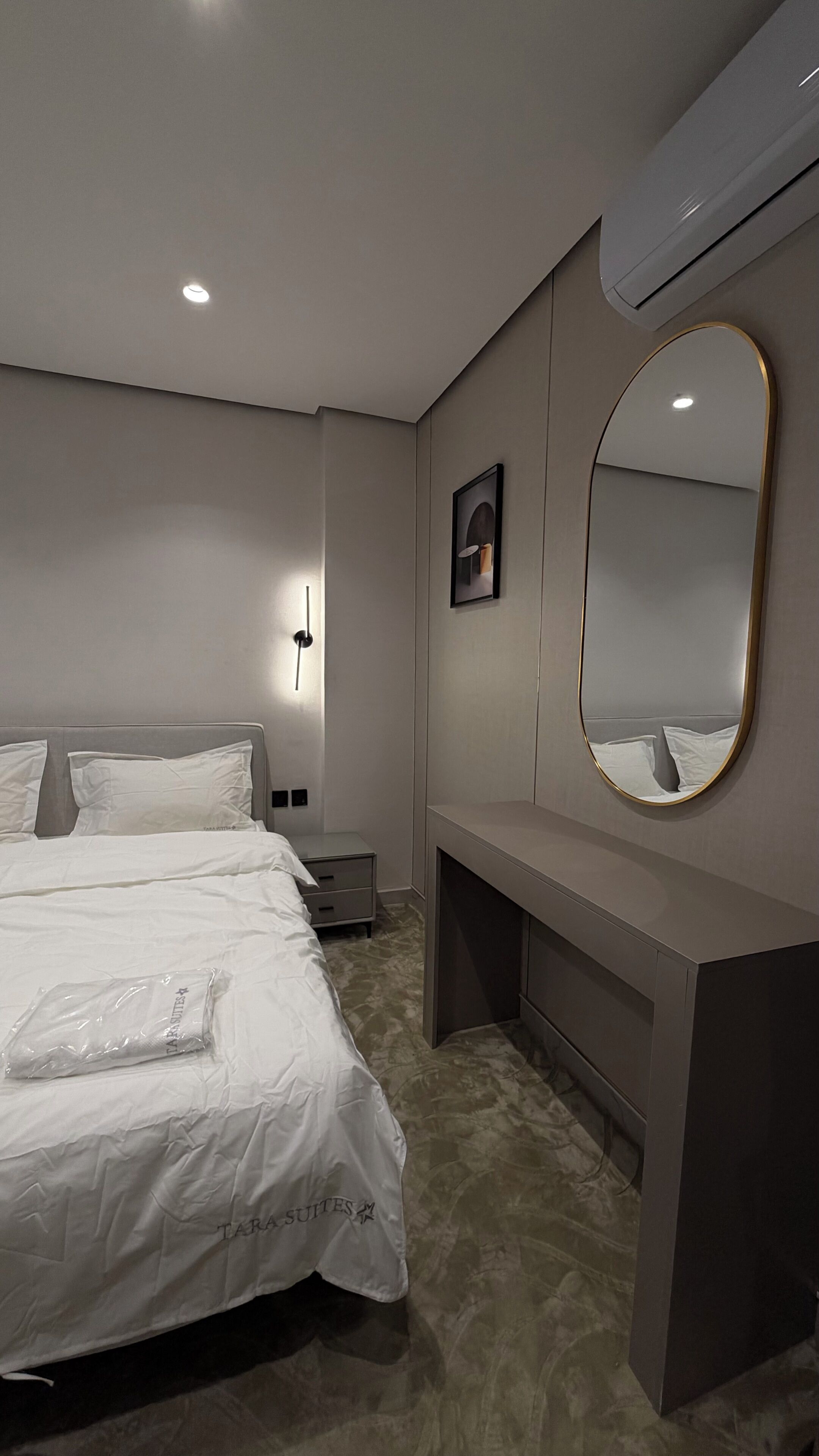 A hotel room with a bed, a bedside table, a mirror, and a wall-mounted picture.