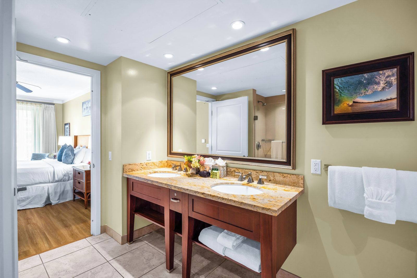 A hotel bathroom with two sinks, a large mirror, and a painting on the wall.