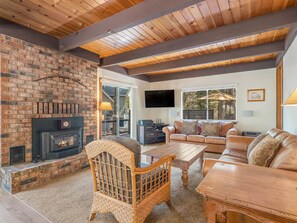 A living room with a brick fireplace, wooden ceiling beams, a television, a sofa, and a coffee table.