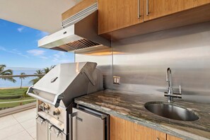 An outdoor kitchen with a stainless steel range, a sink, and wooden cabinets. - Honua Kai | Ocean View 7 BR, Sleeps 20 | Car Incl. w/ 6+ Nights | HKK ML-3356 by KBM (Lahaina)