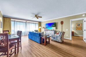 A living room with a dining table, blue sofa, patterned armchair, and a TV. - Honua Kai | Ocean View 7 BR, Sleeps 20 | Car Incl. w/ 6+ Nights | HKK ML-3356 by KBM (Lahaina)