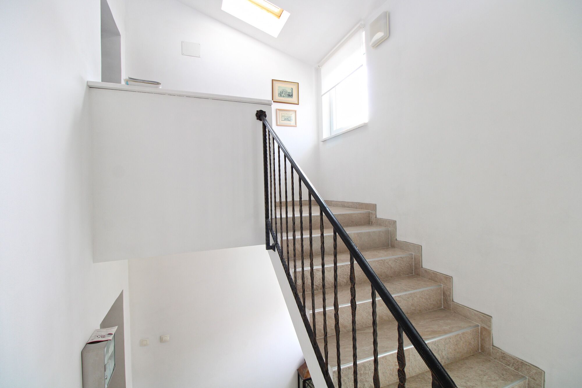 Un escalier avec une rampe noire, des marches de couleur beige et des murs blancs.