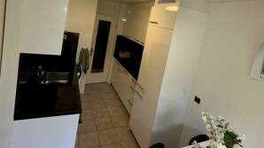 A compact kitchen with white cabinets, a black countertop, and a small sink. There is a white table with a vase of flowers and a piece of paper on it. - Furnished Apartment in Baden (Baden)