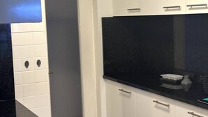 A kitchen with white cabinets, a black countertop, and a stainless steel sink. - Furnished Apartment in Baden (Baden)