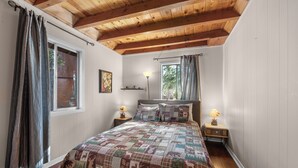Een slaapkamer met een houten plafond, een gewatteerde sprei, twee bedlampen en een raam met gordijnen.