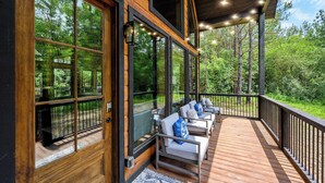 A wooden deck with outdoor seating, large windows, and a view of the forest. - Modern Glass Cabin w/ Hot Tub & Outdoor Lounge (Broken Bow)