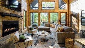 A spacious living room with a fireplace, large windows, and a cozy seating area. - Modern Glass Cabin w/ Hot Tub & Outdoor Lounge (Broken Bow)