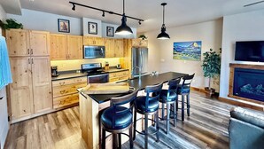A modern kitchen with wooden cabinets, a central island with bar stools, a microwave, a refrigerator, and a dining table.