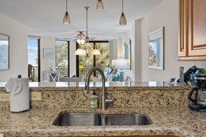 Una cocina con encimeras de granito, pileta de acero inoxidable, luces colgantes y vista al exterior.