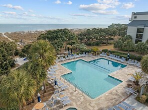 Una piscina con sillas de descanso y sombrillas, rodeada de palmeras y vista a la playa.