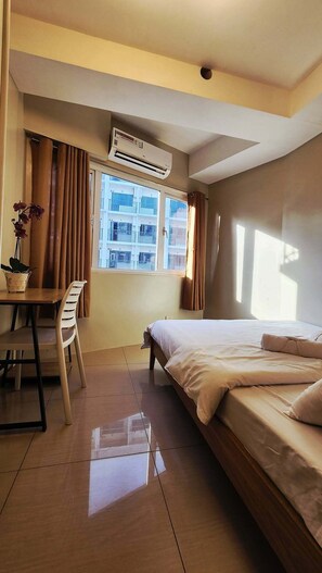 Ein Hotelzimmer mit einem Bett, einem Schreibtisch, einem Stuhl, einer Klimaanlage und einem fenster mit Vorhängen.