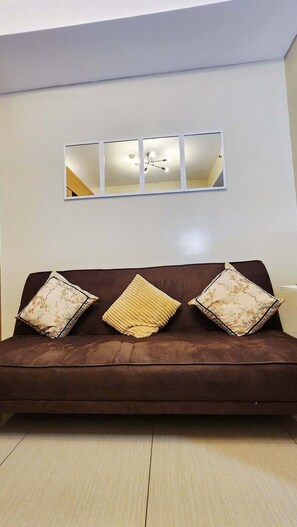 Ein braunes Sofa mit drei gemusterten Kissen und einem darüber hängenden Wandspiegel.