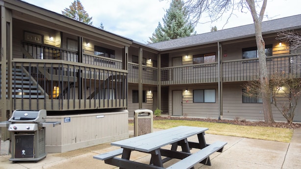 A building with a patio area featuring a grill, a picnic table, and a trash can. - Marina Cay Condo | Sleeps 4 | Steps from Flathead Lake, Bigfork Village & Glacier Country (Bigfork)