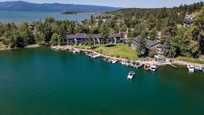 A lakeside property with multiple buildings, a dock with boats, and a clear view of the lake and mountains in the background. - Marina Cay Condo | Sleeps 4 | Steps from Flathead Lake, Bigfork Village & Glacier Country (Bigfork)