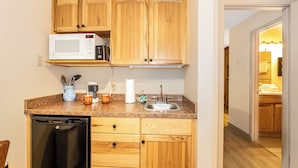 A compact kitchen with wooden cabinets, a microwave, a sink, and a dishwasher. - Marina Cay Condo | Sleeps 4 | Steps from Flathead Lake, Bigfork Village & Glacier Country (Bigfork)