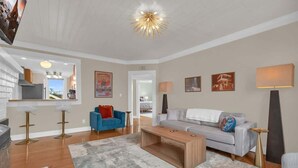 Una sala de estar moderna con sofá, mesa de centro y taburetes de bar. Se ve una zona de cocina al fondo.