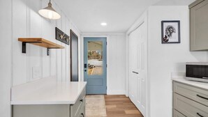 A kitchen with a white countertop, wooden shelves, a blue door, and a framed picture on the wall.