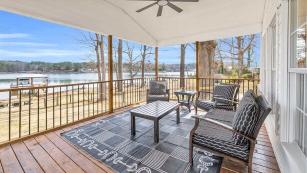 A covered porch with a ceiling fan, outdoor seating, and a view of a lake.