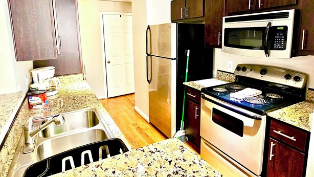A kitchen with a stainless steel sink, a microwave, an oven, and dark wooden cabinets. - Convenience-Downtown-MedCtr-Entertainment-Westheimer-NRG (Houston)