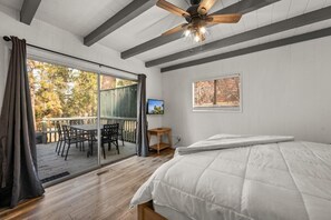 Un dormitorio con cama, ventilador de techo, puerta corrediza de vidrio que da a un patio exterior y una pequeña mesa con silla.