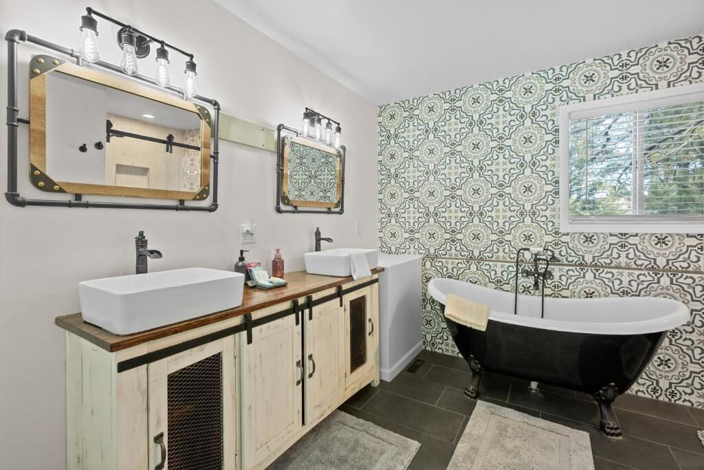 Une salle de bain avec une baignoire sur pieds, deux lavabos, un grand miroir et des murs recouverts de carreaux à motifs.