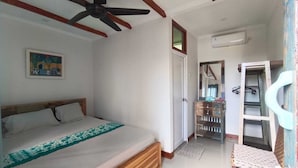 A bedroom with a bed, a ceiling fan, a painting, and a bathroom with a shower and a towel rack.