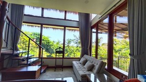 A room with a staircase, a sofa, and large windows offering a view of greenery.