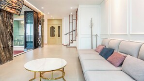 A modern living room with a white sofa, a round coffee table, and a staircase leading to another level. - Ganghwa Elijah Pool Villa (Incheon)