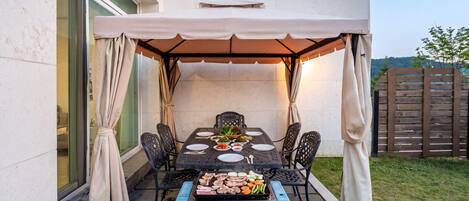 An outdoor patio with a covered table, chairs, and a grill.