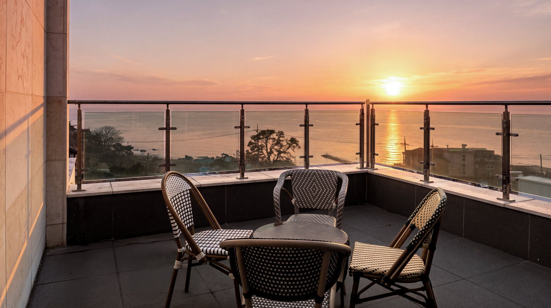 A balcony with a table and chairs overlooking a sunset over the sea.
