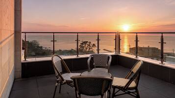 A balcony with a table and chairs overlooking a sunset over the sea.