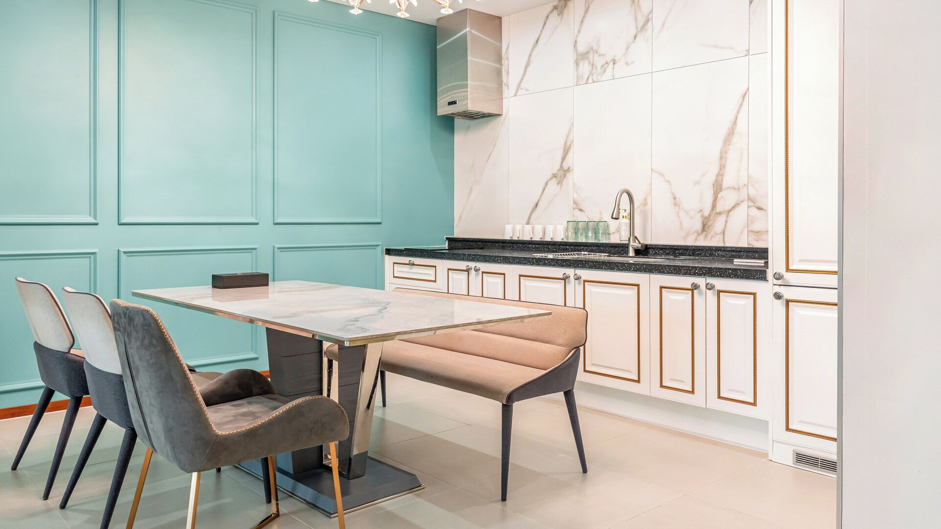 Una cucina moderna con pareti color petrolio, zoccolo di marmo e zona pranzo con tavolo di marmo e sedie imbottite.
