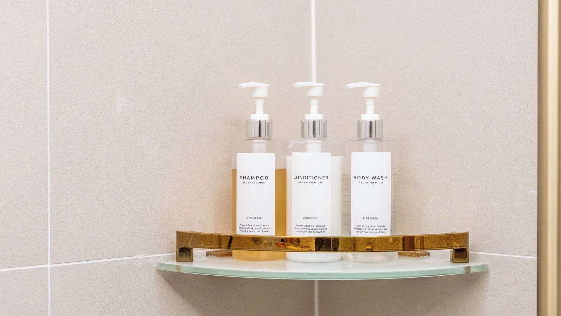 Three bottles of Arder Premium products on a glass shelf in a bathroom.