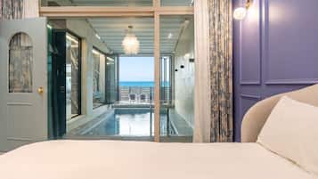 A room with a bed, a view of a pool, and a balcony with a railing.