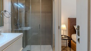 Een moderne badkamer met een douchecabine van glas, een witte wastafel en een nachtkastje met een lamp.