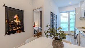 Een modern interieur met een eettafel, een groot schilderij in een lijst, een potplant en een keukenhoek.