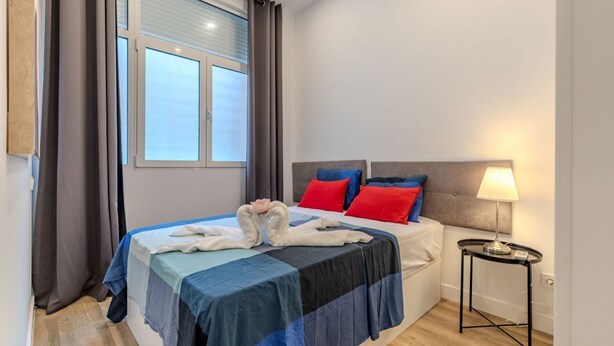 Een slaapkamer met een bed, nachtkastje, lamp en raam met gordijnen.