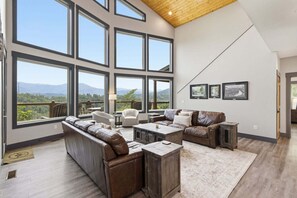 A spacious living room with large windows, a high ceiling, and a view of mountains. - Viewtopia - Luxury Smoky Mountain Cabin in Gatlinburg | Views, Hot Tub, Firepit & Game Loft (Gatlinburg)