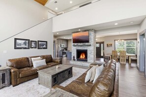A spacious living room with a fireplace, leather sofas, a coffee table, and framed pictures on the wall. - Viewtopia - Luxury Smoky Mountain Cabin in Gatlinburg | Views, Hot Tub, Firepit & Game Loft (Gatlinburg)