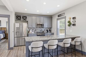 A modern kitchen with grey cabinets, stainless steel appliances, and a granite island with bar stools. - Viewtopia - Luxury Smoky Mountain Cabin in Gatlinburg | Views, Hot Tub, Firepit & Game Loft (Gatlinburg)