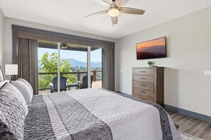 Et soveværelse med en stor seng, ventilator, fjernsyn, kommode og en balkon med udsigt til bjerge.