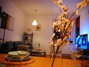 A dining table with wine glasses, a vase with flowers, a television, and a cozy seating area with cushions. - Spacious, designer 3-room apartment in  center of warsaw (Warszawa)