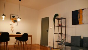 Een moderne woonkamer met een glazen salontafel, een bank, een eettafel met stoelen en een boekenkast.