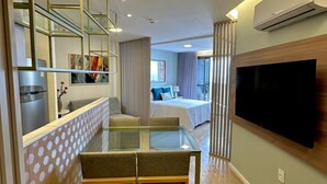 Et moderne hotelværelse med et glasbord, en sofa, et fjernsyn ophængt på væggen og et tekøkken.