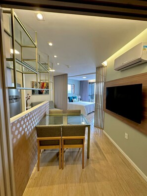 Una moderna camera d'albergo con un tavolo da pranzo in vetro, una poltrona, una TV a parete e un angolo cottura.
