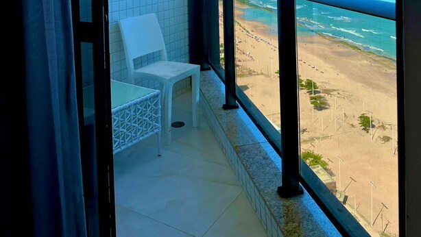 En balkon med udsigt over stranden, en hvid stol og fliserede vægge.